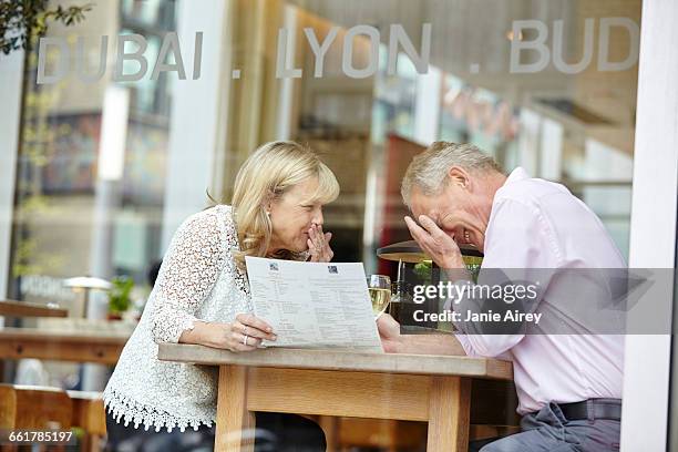 mature dating couple giggling at restaurant table - awkward date stock-fotos und bilder