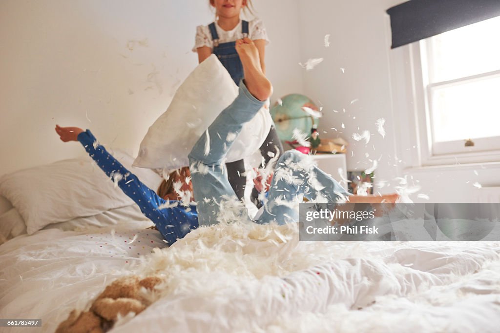 Two sister having feather pillow fight on bed