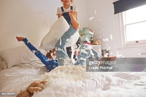 two sister having feather pillow fight on bed - girls wrestling stockfoto's en -beelden