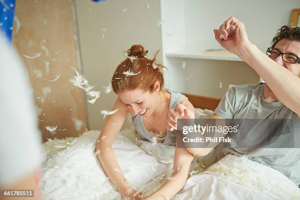 mid adult couple having pillow fight with daughter in bed - kissenschlacht paar stock-fotos und bilder