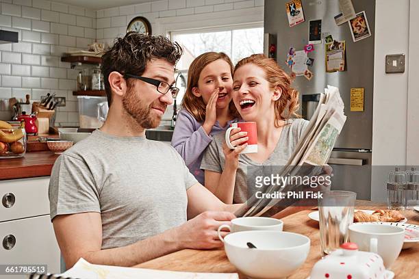 mid adult man at breakfast table reading newspaper whilst daughter and mother laughing - smart kitchen fotografías e imágenes de stock