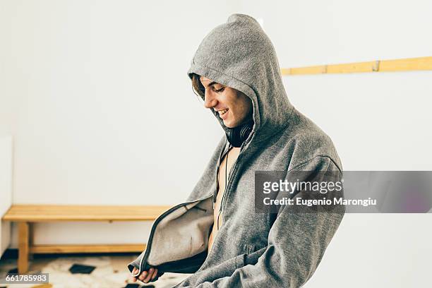 man zipping up hooded top looking down smiling - hood clothing stock pictures, royalty-free photos & images