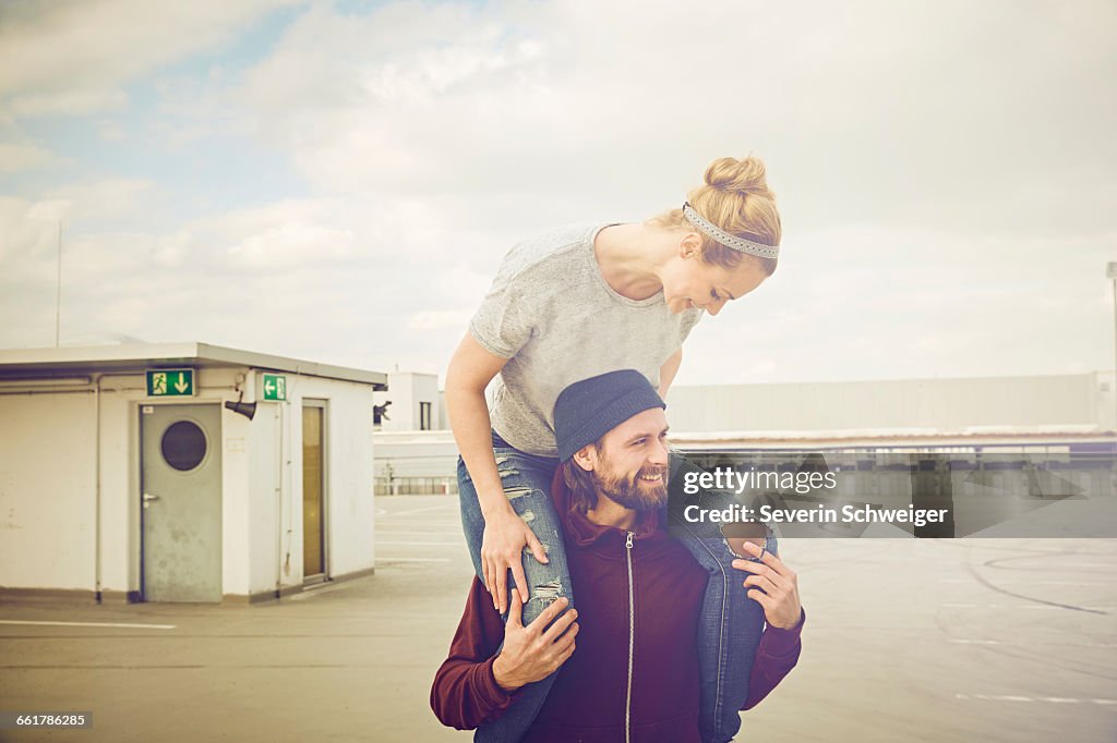 Mid adult woman getting shoulder ride from boyfriend on rooftop parking lot