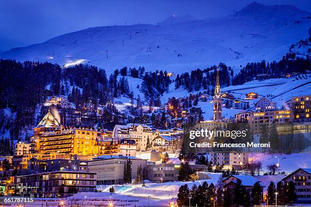 village beneath mountain on snow covered landscape illuminated in the evening, sankt moritz, switzerland - st moritz stock pictures, royalty-free photos & images