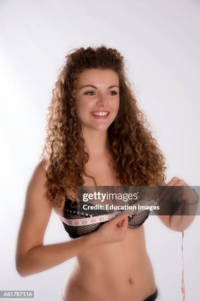 Teenage girl holding a tape measure over her bra to check her bust size in inches.