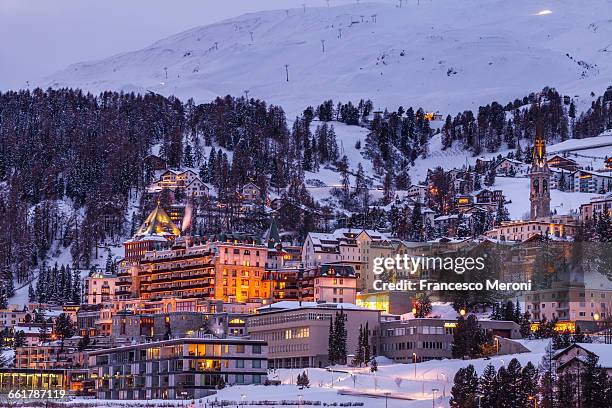 village beneath mountain on snow covered landscape illuminated in the evening, sankt moritz, switzerland - saint moritz stock-fotos und bilder