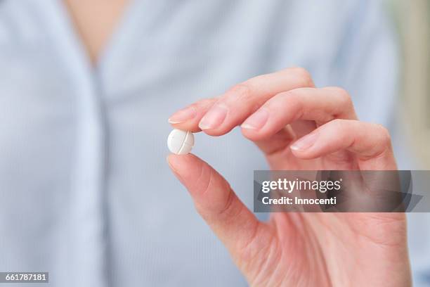 womans hand holding pill between thumb and forefinger - pillole foto e immagini stock