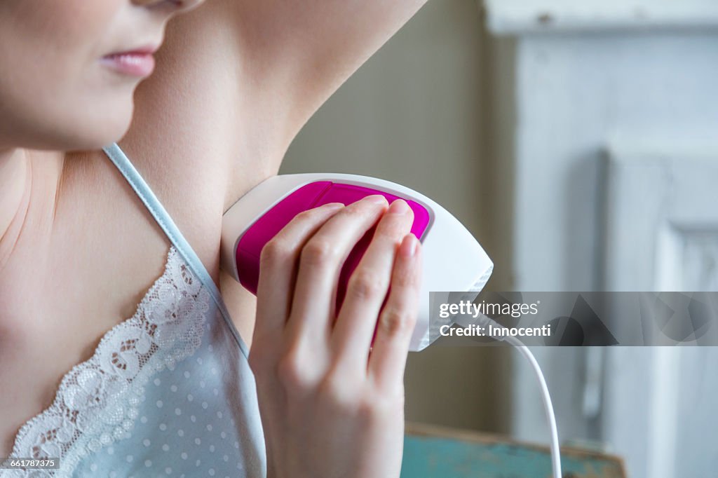 Cropped view of woman using electric shaver to shave armpit