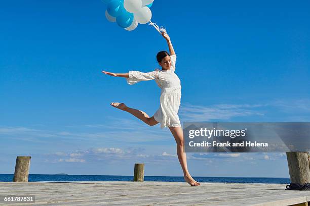 young woman dancing on wooden pier, holding bunch of balloons - blue dress imagens e fotografias de stock