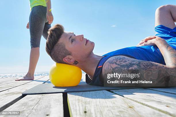 tattooed man lying on pier using ball as pillow - pompadour imagens e fotografias de stock