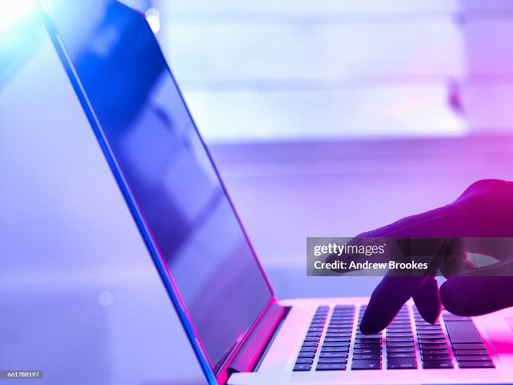 Gloved hand hacking laptop computer