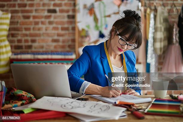 woman in design studio sitting at desk sketching fashion design - 品牌服裝 個照片及圖片檔