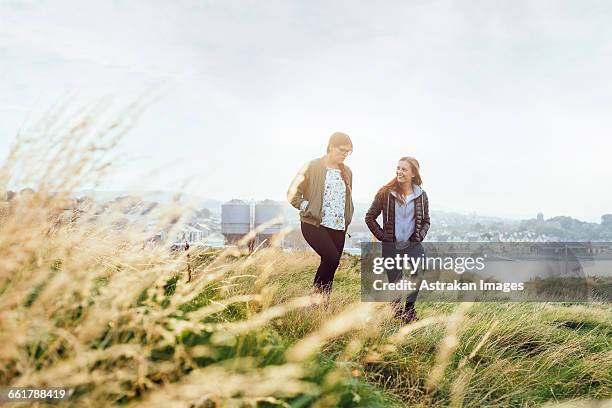 happy female friends talking while walking on grassy hill against sky - verwaltungsbezirk county wicklow stock-fotos und bilder