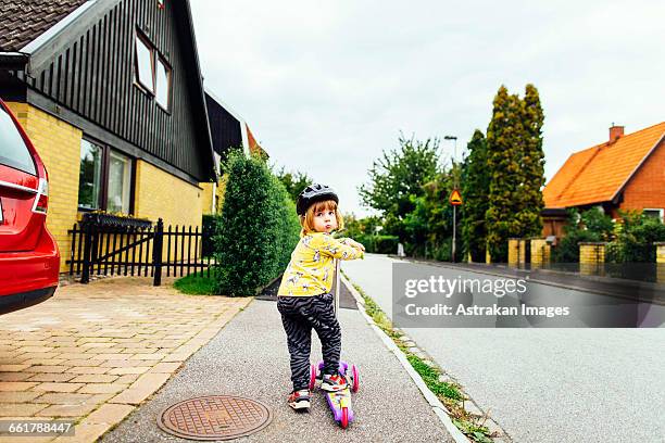 rear view of girl riding push scooter on sidewalk - kinder kickboard stock-fotos und bilder