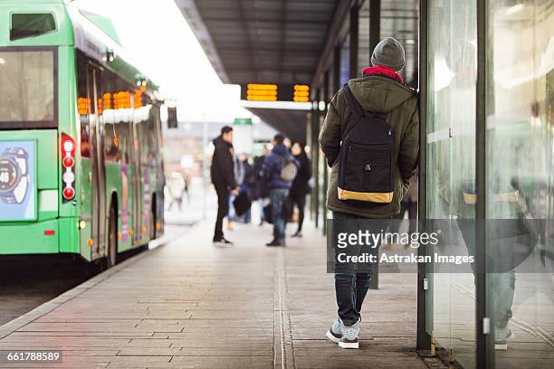 rear view of man waiting at bus stop - waiting foto e immagini stock