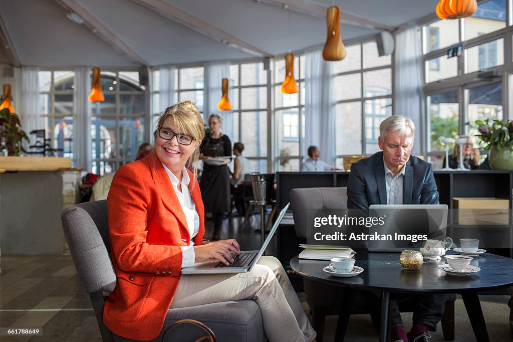 Male and female business colleague using laptops in restaurant