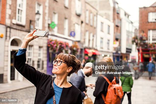 smiling woman taking selfie with friends standing in background on city street - dublin imagens e fotografias de stock