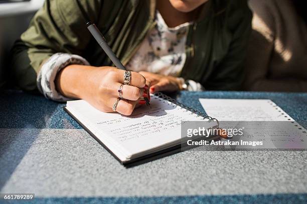 midsection of businesswoman writing on diary in train - journal stockfoto's en -beelden