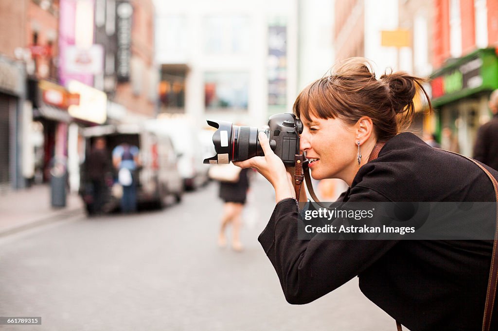 Side view of woman photographing on city street