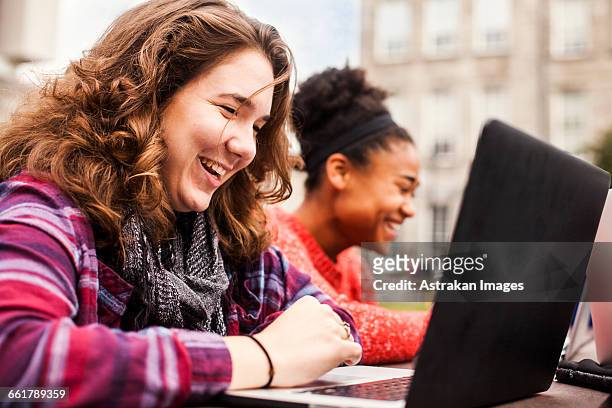 happy female student using laptop with friend in background at campus - trinity college dublin stock pictures, royalty-free photos & images