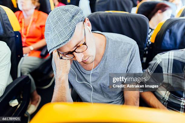 businessman listening music while sleeping in airplane - man sleeping with cap stock pictures, royalty-free photos & images