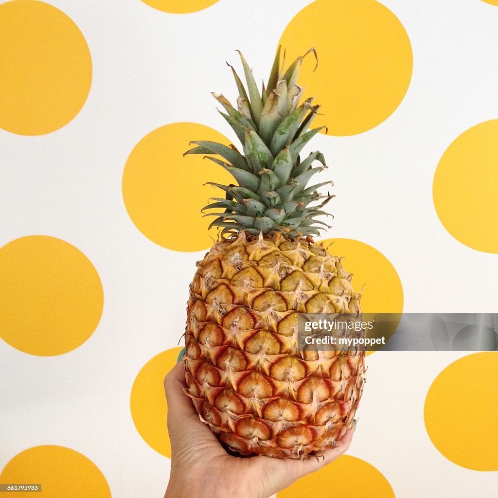 Woman holding pineapple in front of  yellow spot background