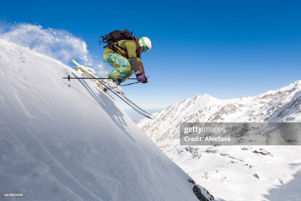 Male skier skiing off piste and jumping in air