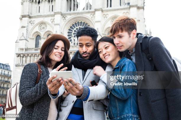 quattro giovani amici multietnici si divertono a posare per selfie sotto il sole primaverile insieme da notre dame a parigi - île de la cité foto e immagini stock