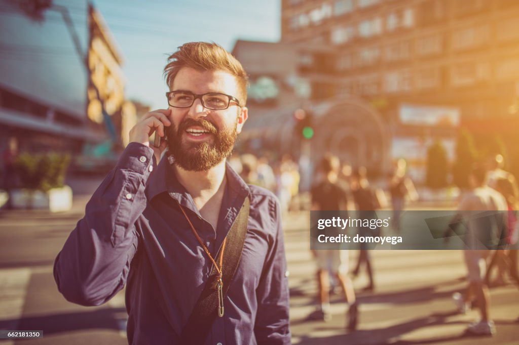 Cheerful businessman using phone in the city street