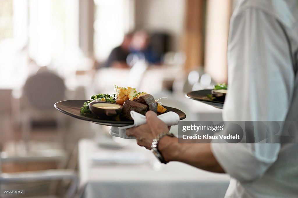 Close-up of waiter walkiing with dishes