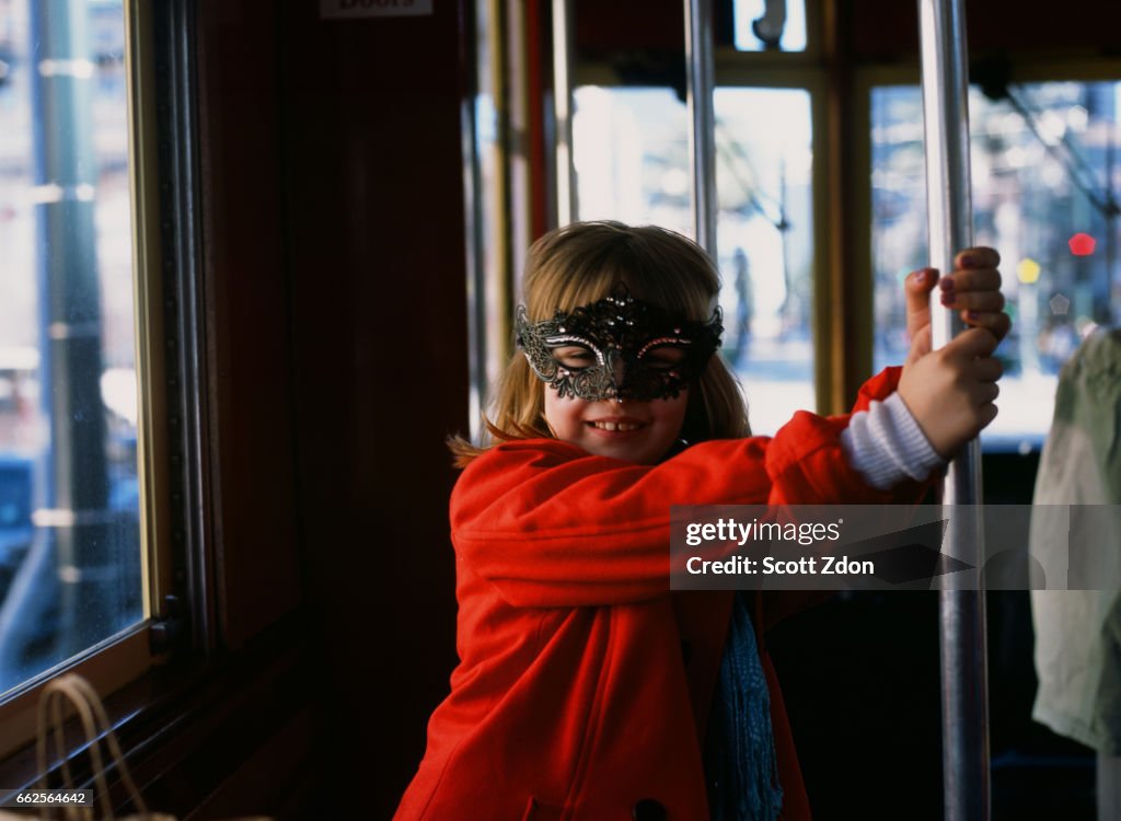 Young girl on New Orleans streetcar wearing Mardi Gras mask