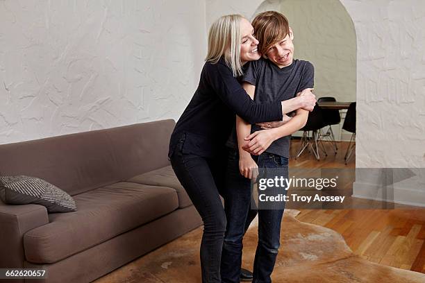 mother giving son a big hug in living room. - troy bond stock pictures, royalty-free photos & images