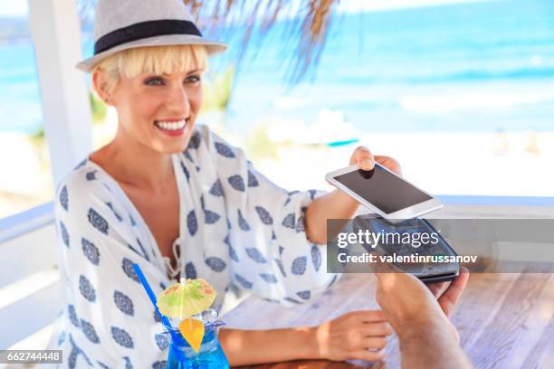 lächelnde blonde frau mit smartphone für mobiles bezahlen - apple pay mobile payment stock-fotos und bilder