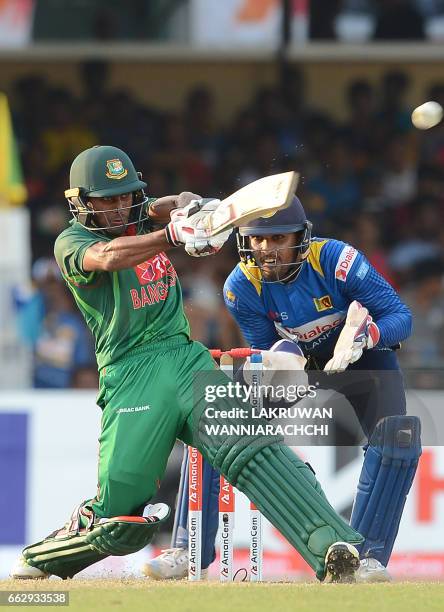 Bangladesh cricketer Mehedi Hasan is watched by Sri Lankan wicketkeeper Dinesh Chandimal as he plays a shot during the third and final one day...