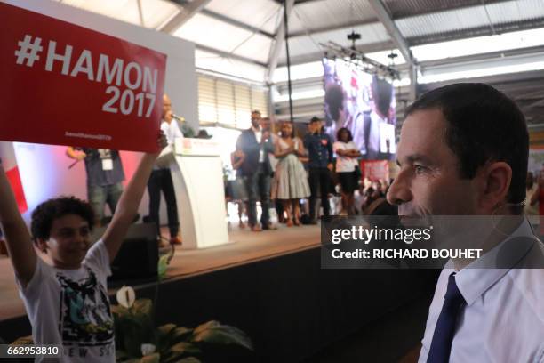 French presidential election candidate for the left-wing French Socialist party Benoit Hamon looks on as a child holds a banner in his support in...