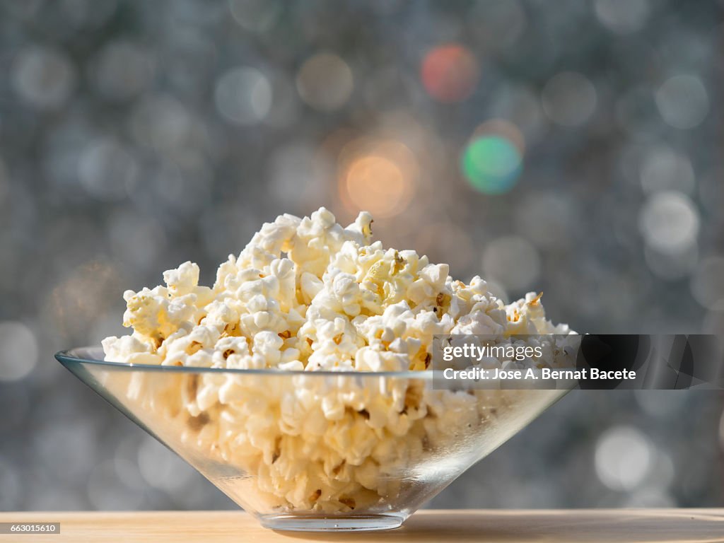 Bowl of popcorn, on a wooden table lit by sunlight