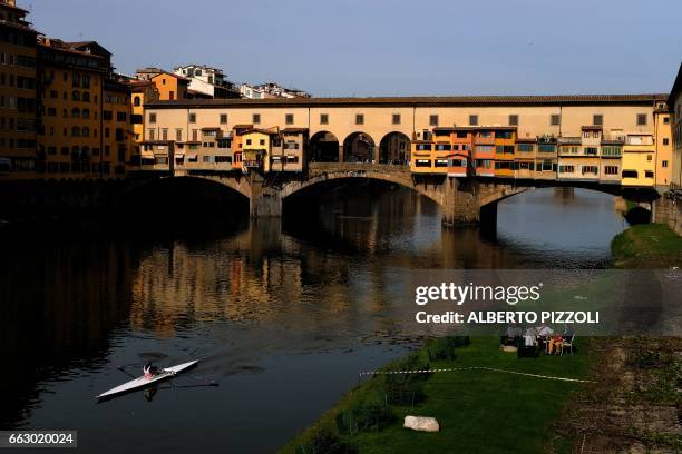 People relax on the banks of the river Arno with the Ponte Vecchio in the background, on April 1, 2017 in Florence. / AFP PHOTO / Alberto PIZZOLI