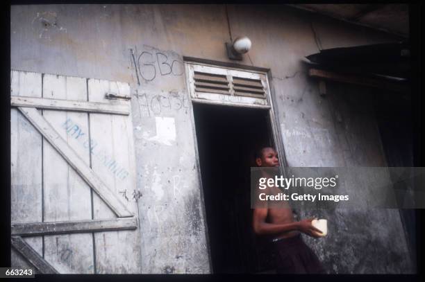 Man stands in front of a home December 15, 1999 in the Ajegunle area of Lagos, Nigeria. Signs painted on the fronts of the houses indicate that the...
