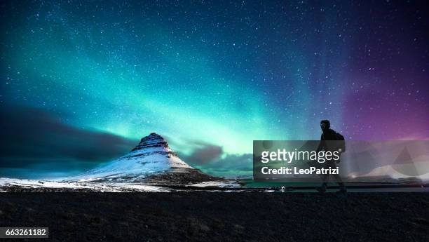 northern lights in mount kirkjufell iceland with a man passing by - awe imagens e fotografias de stock