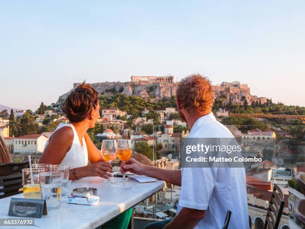 couple drinking in front of the acropolis at sunset. athens, greece - athens greece - fotografias e filmes do acervo