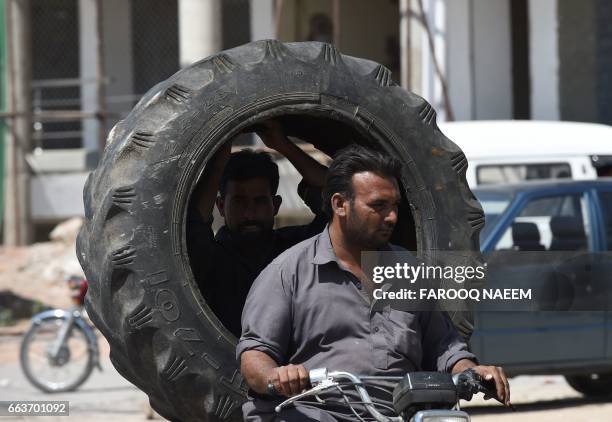 Pakistani labourers transport a tyre on a motorcycle at a market in Rawalpindi on April 2, 2017. / AFP PHOTO / FAROOQ NAEEM