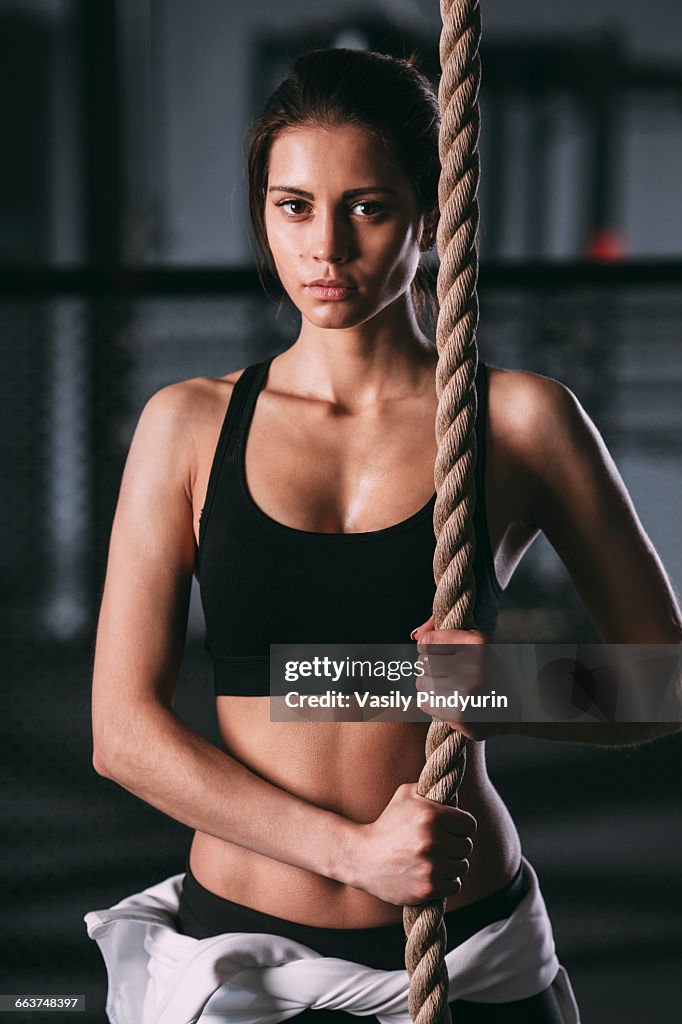 Portrait of confident young woman exercising with rope at gym