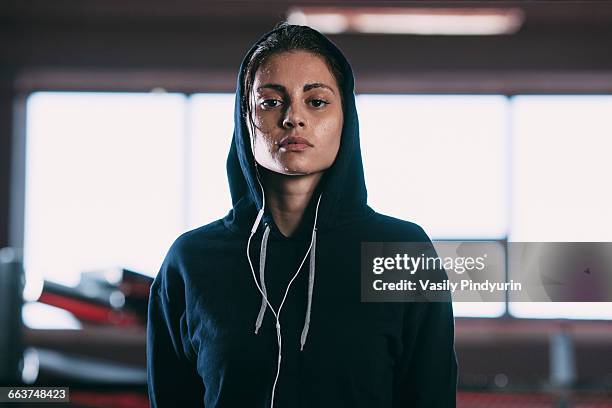 portrait of tired woman wearing hooded shirt standing at gym - atlet stock-fotos und bilder