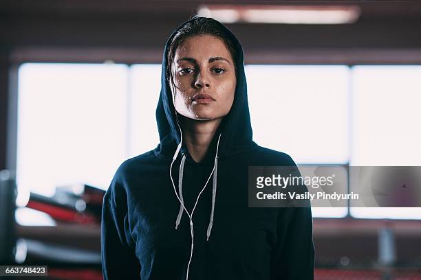 portrait of tired woman wearing hooded shirt standing at gym - posizione sportiva foto e immagini stock