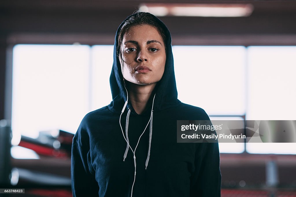 Portrait of tired woman wearing hooded shirt standing at gym