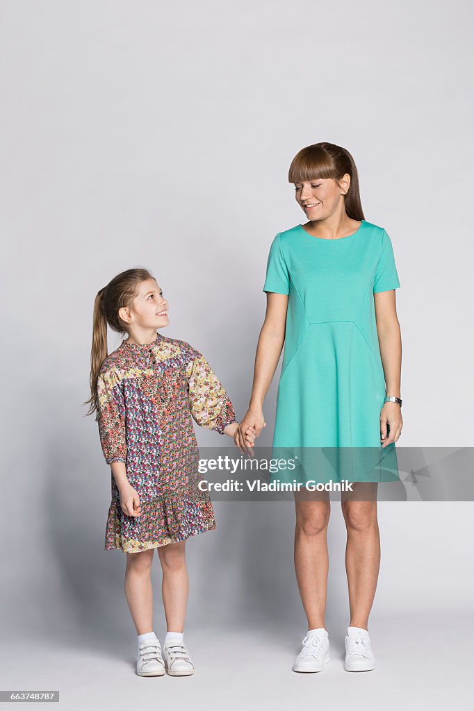 Happy mother and daughter holding hands against white background