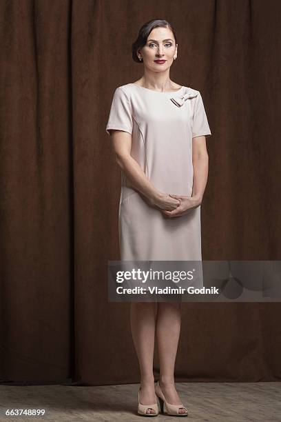 portrait of confident beautiful woman standing against brown curtain in studio - vestito marrone foto e immagini stock