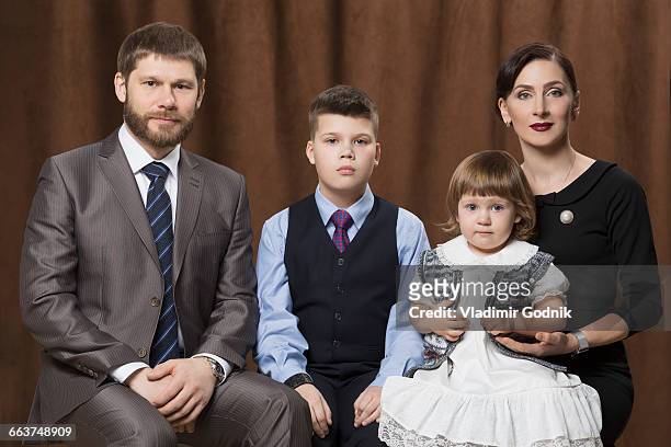 portrait of family sitting against brown curtains in studio - formal portrait stock-fotos und bilder