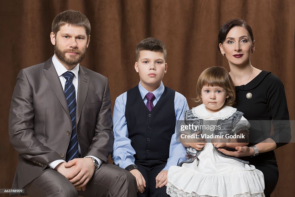 Portrait of family sitting against brown curtains in studio