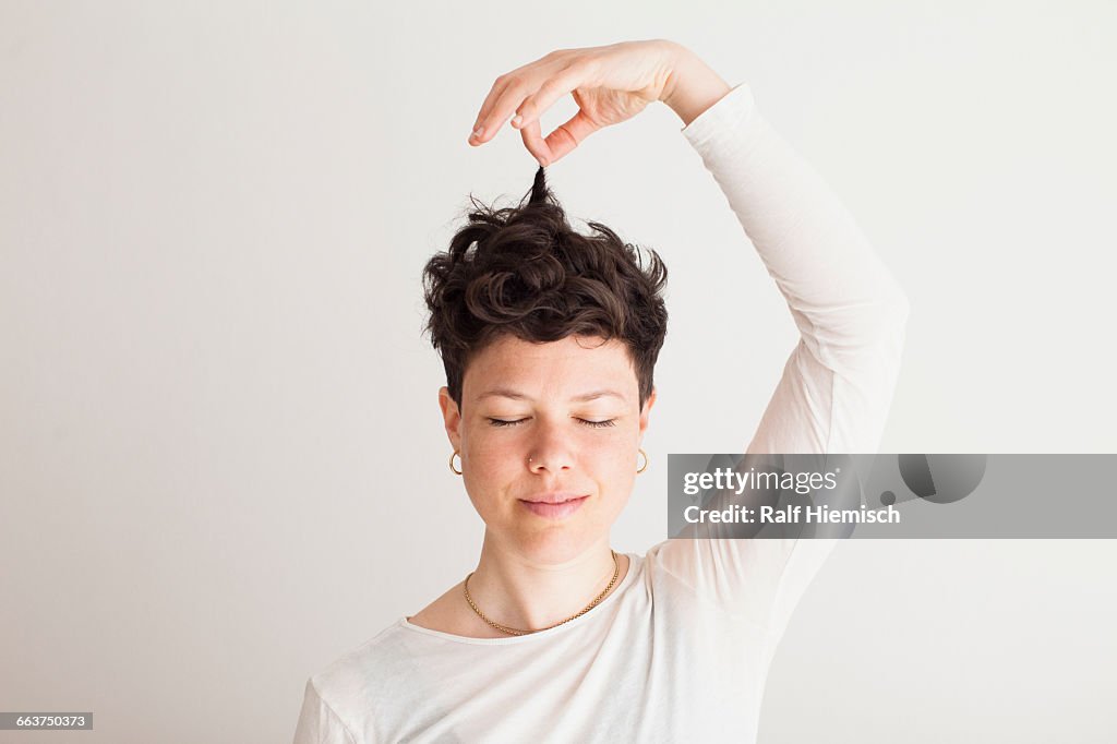 Close-up of happy mid adult woman holding her hair against white background